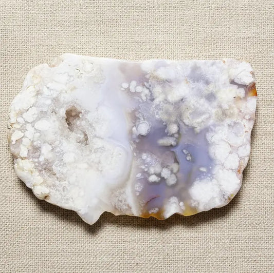 A raw flower agate geode stone slice with white, cloudy outer matrix and a translucent lavender-purple interior cavity 