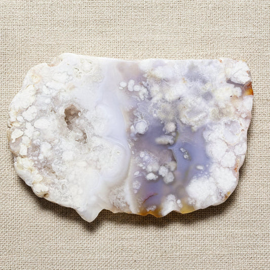 A raw flower agate geode stone slice with white, cloudy outer matrix and a translucent lavender-purple interior cavity 
