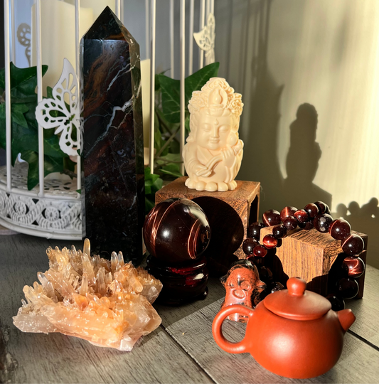 Still life with crystals, a Buddha statue, prayer beads, and a small teapot on a wooden surface.