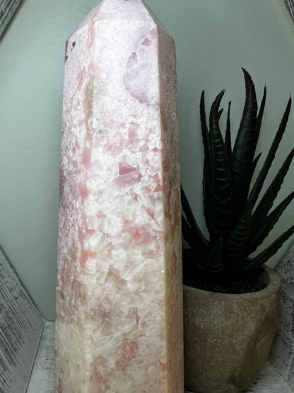A tall, pink crystal tower next to a potted snake plant.