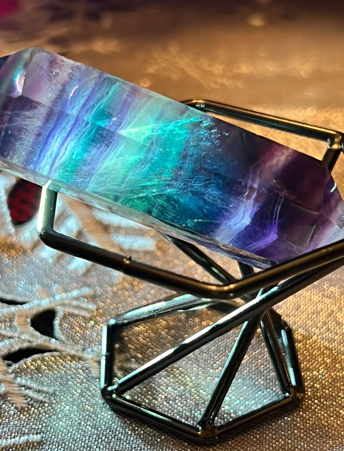Fluorite crystal tower in black metal stand on sparkling fabric.