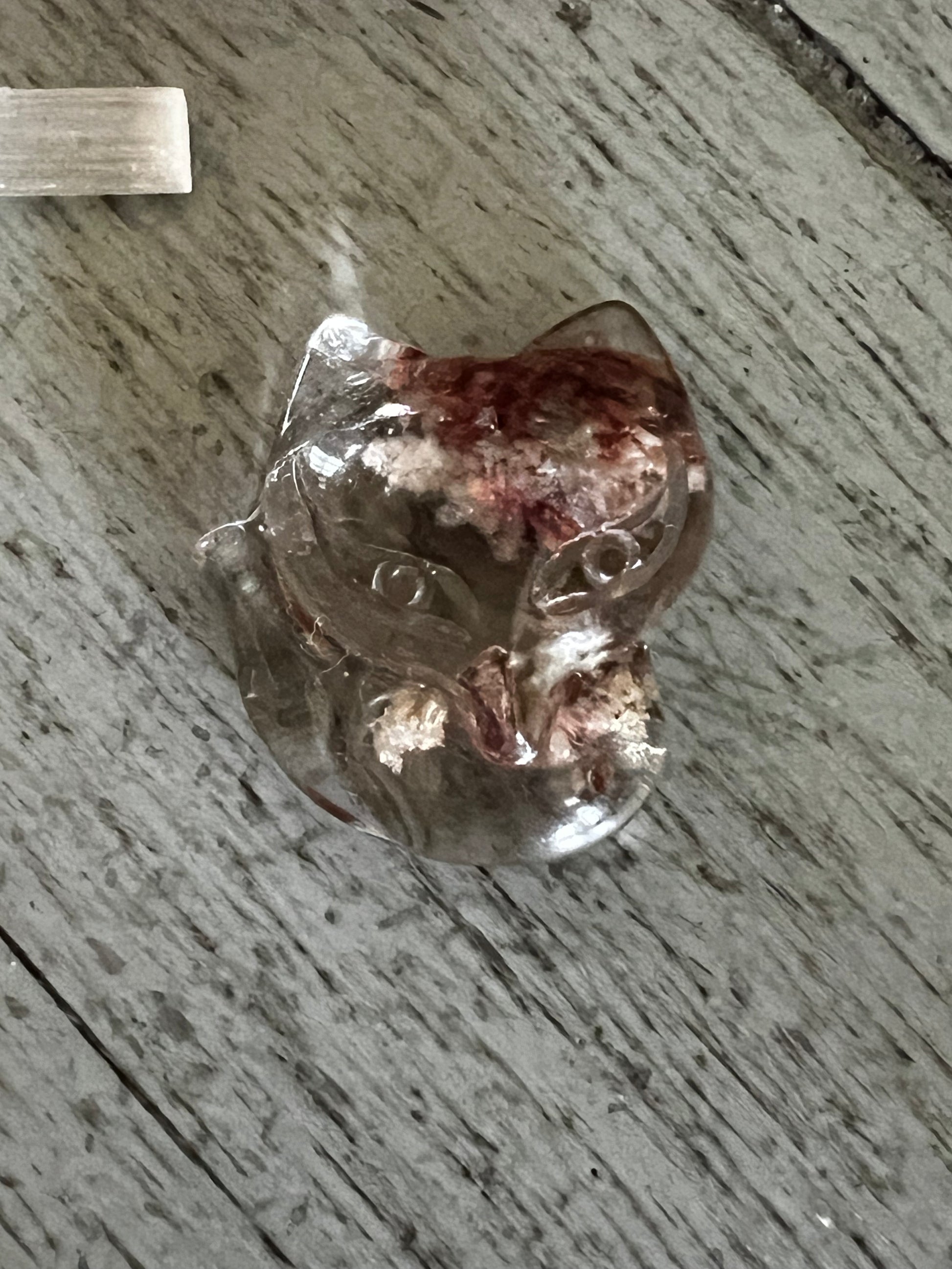 Crystal cat figurine with red and white inclusions on a gray wood surface.