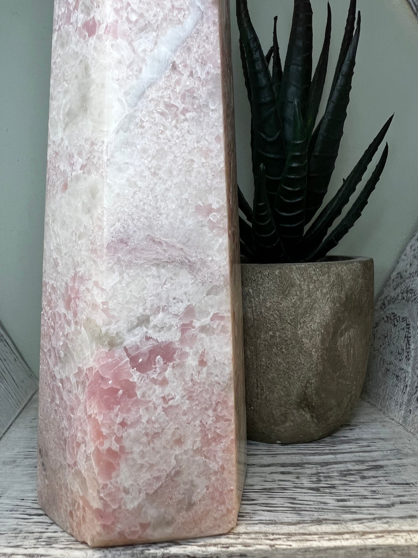 Pink and white stone sculpture next to a potted succulent on a weathered white shelf.