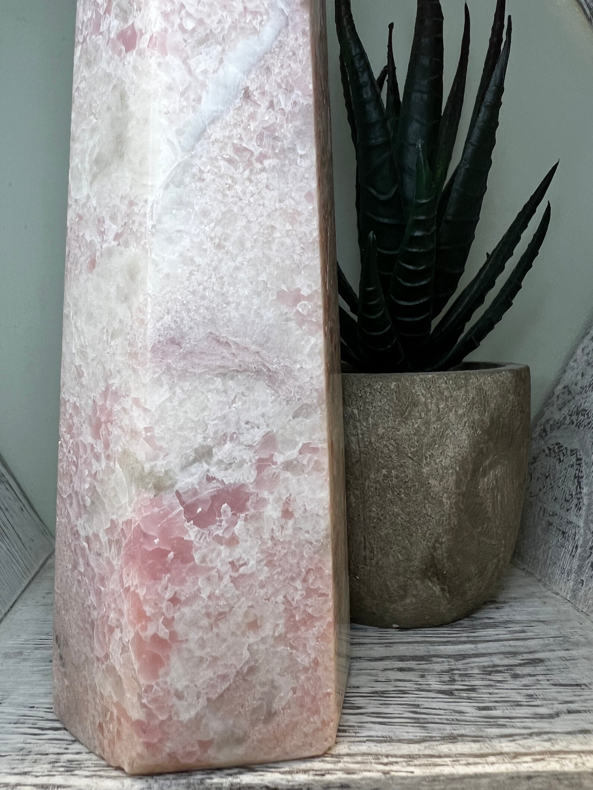 Pink and white stone sculpture next to a potted succulent on a weathered white shelf.