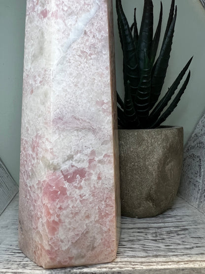 Pink and white stone sculpture next to a potted succulent on a weathered white shelf.