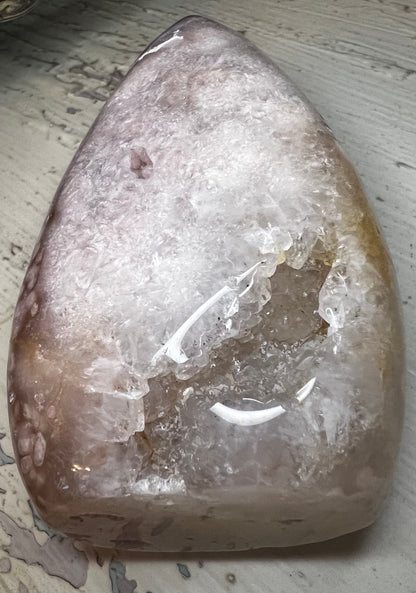 A polished crystal geode with pink and white hues, featuring a prominent cavity with clear crystalline formations.