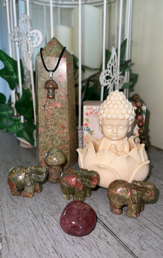 Still life of crystals including a tower, a Buddha figure in a lotus flower, small elephant carvings, and a mushroom pendant necklace.