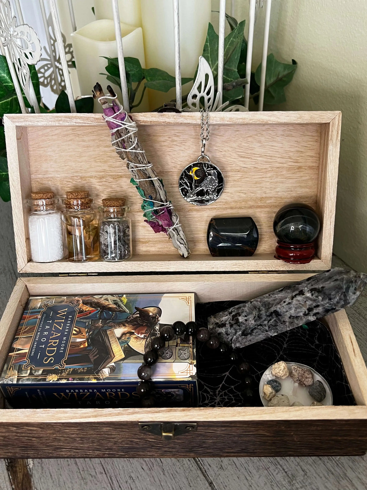 Open wooden box with metaphysical items including crystals, sage, tarot cards, and small glass jars.