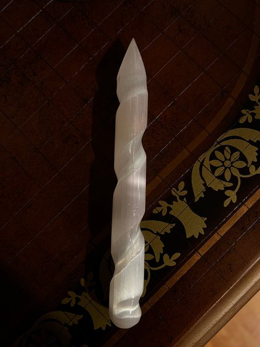 Selenite crystal wand with a spiral design on a brown table.