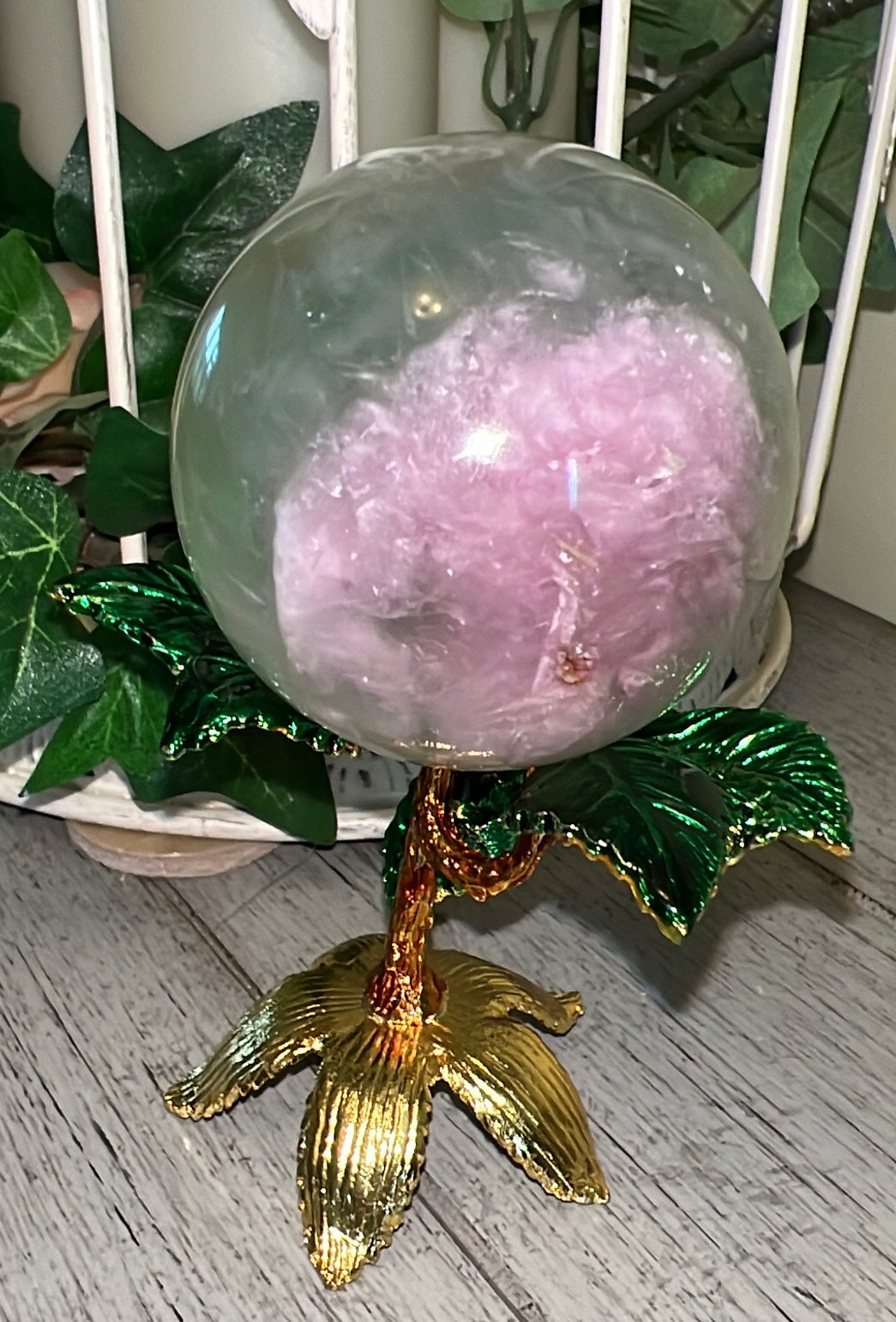 Ornament with a glass orb containing pink fluff, atop a gold and green stand in a plant-like design.
