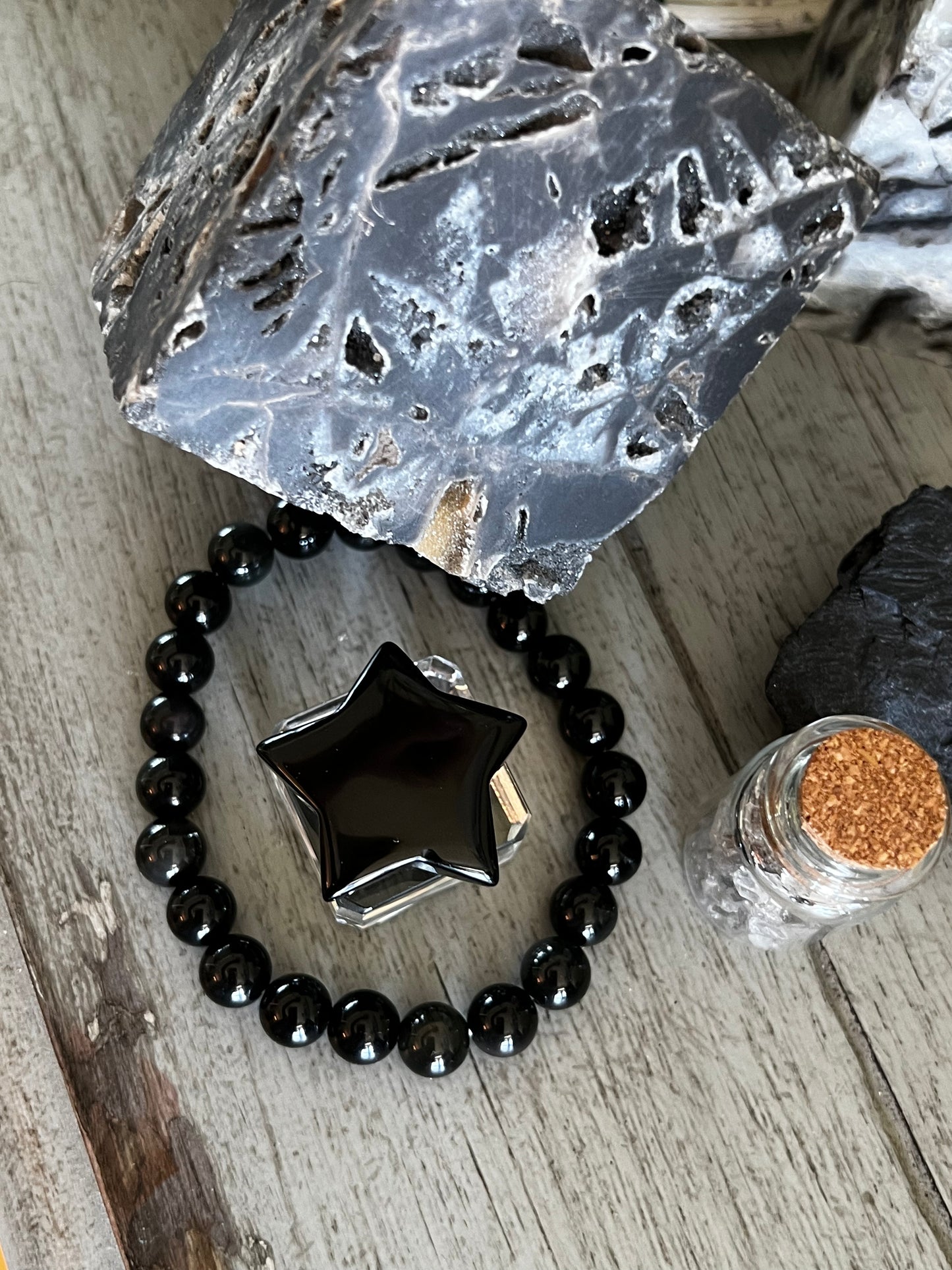 Overhead shot of a black obsidian beaded bracelet with star, crystal, stone, and corked glass jar.