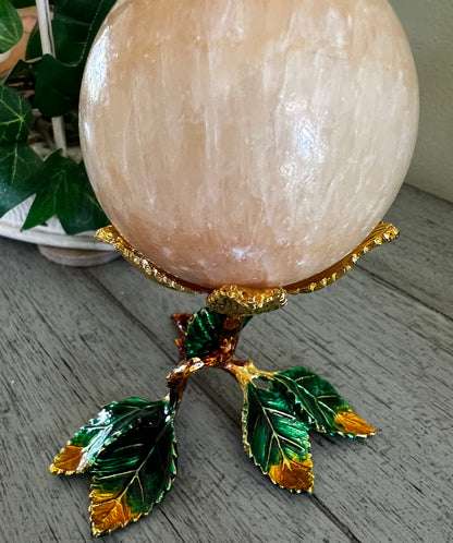 Peach-colored stone sphere on a gold and green leaf stand.