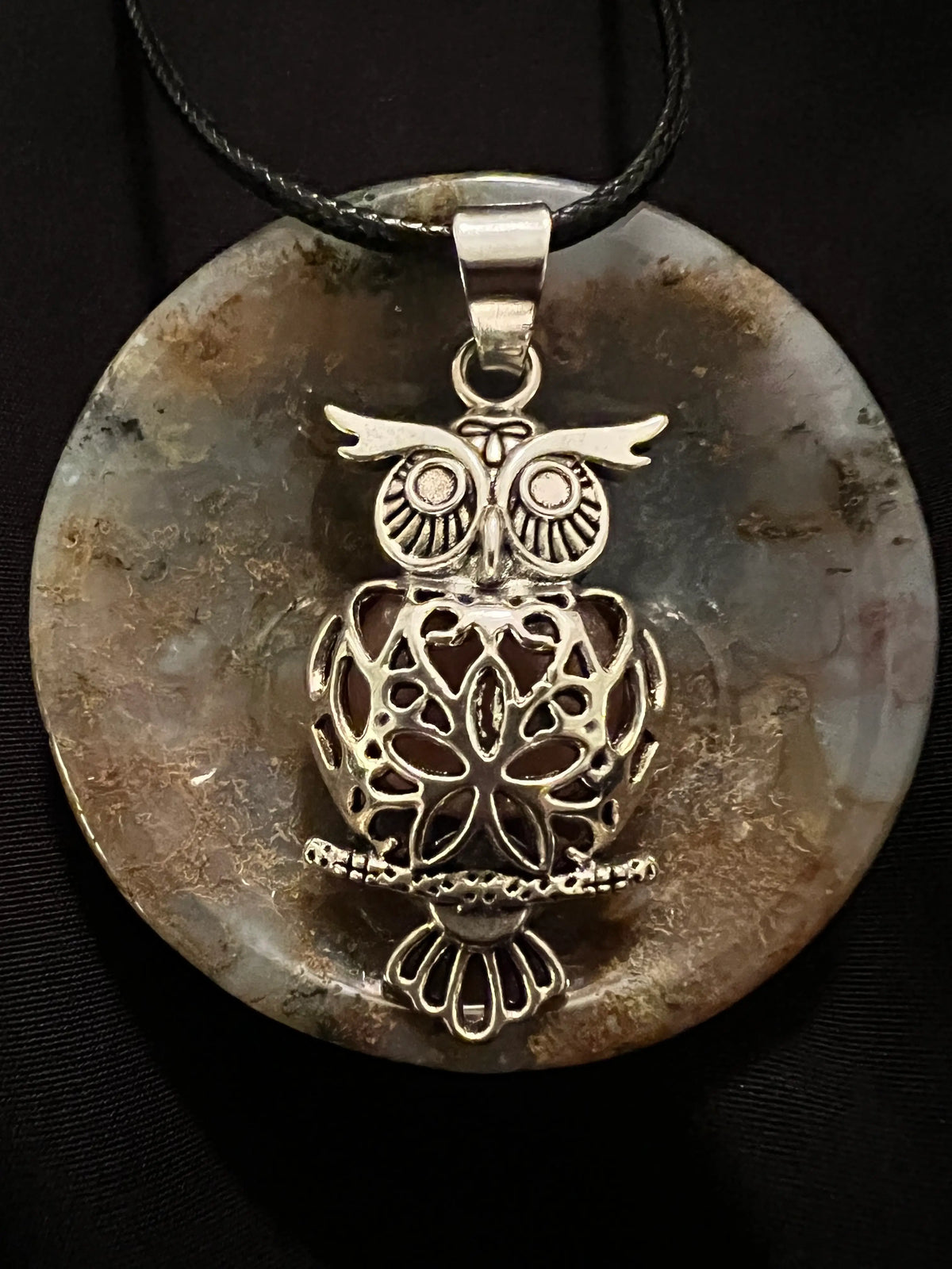 Owl pendant on stone disk with black cord.
