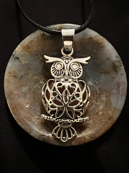 Owl pendant on stone disk with black cord.