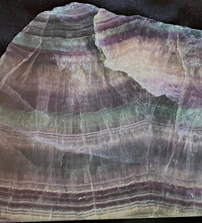 Polished slab of rainbow fluorite with banded patterns in purple, green, and clear hues.
