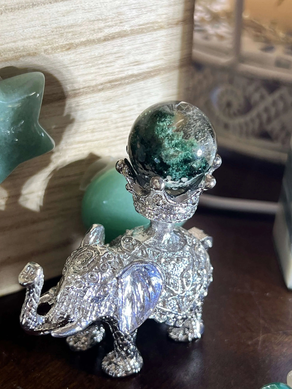 Silver elephant figurine holding a green sphere.
