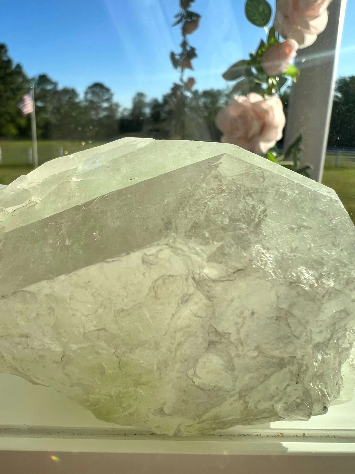 Large light green crystal on a windowsill. Outside, pink roses and an American flag are visible.