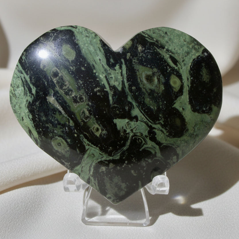 close up of a kambaba jasper carved heart green hues light and dark lime green colors with black swirls on a stand