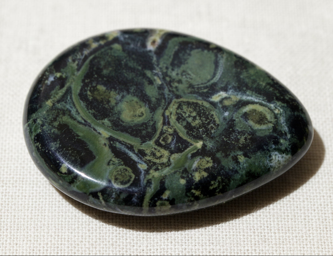 close up of kambaba jasper worry stone bright hues of greens, with black swirls 