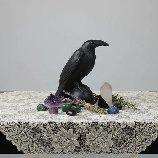 beautiful black obsidian raven carving on a table lace cloth with clear quartz, herbs and tumbles all around