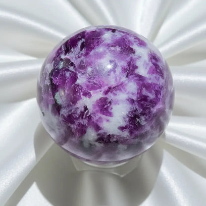 A polished lepidolite purple and white crystal sphere displayed on a clear stand against a light background.