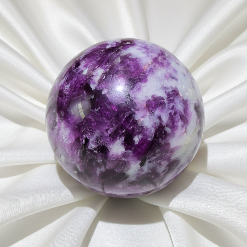 A polished lepidolite purple and white  crystal sphere displayed on a clear stand  
