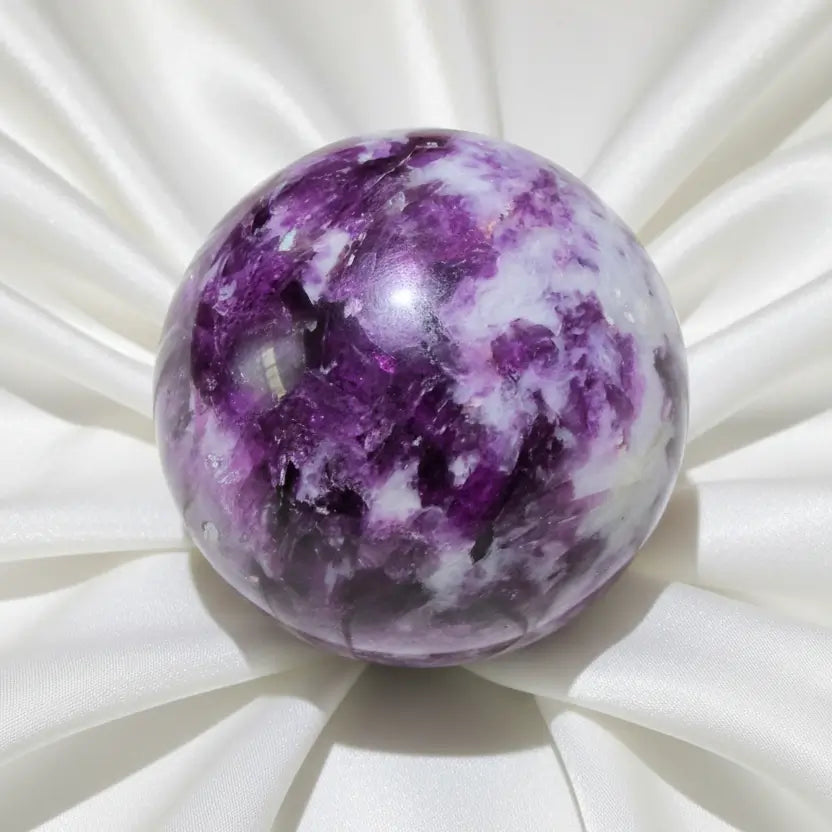A polished lepidolite purple and white  crystal sphere displayed on a clear stand  
