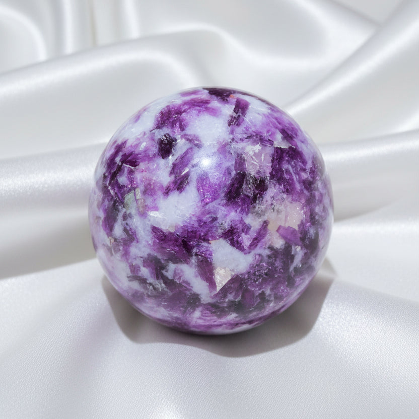 A polished lepidolite crystal sphere with a marbled pattern of purple, white, and pinkish tones