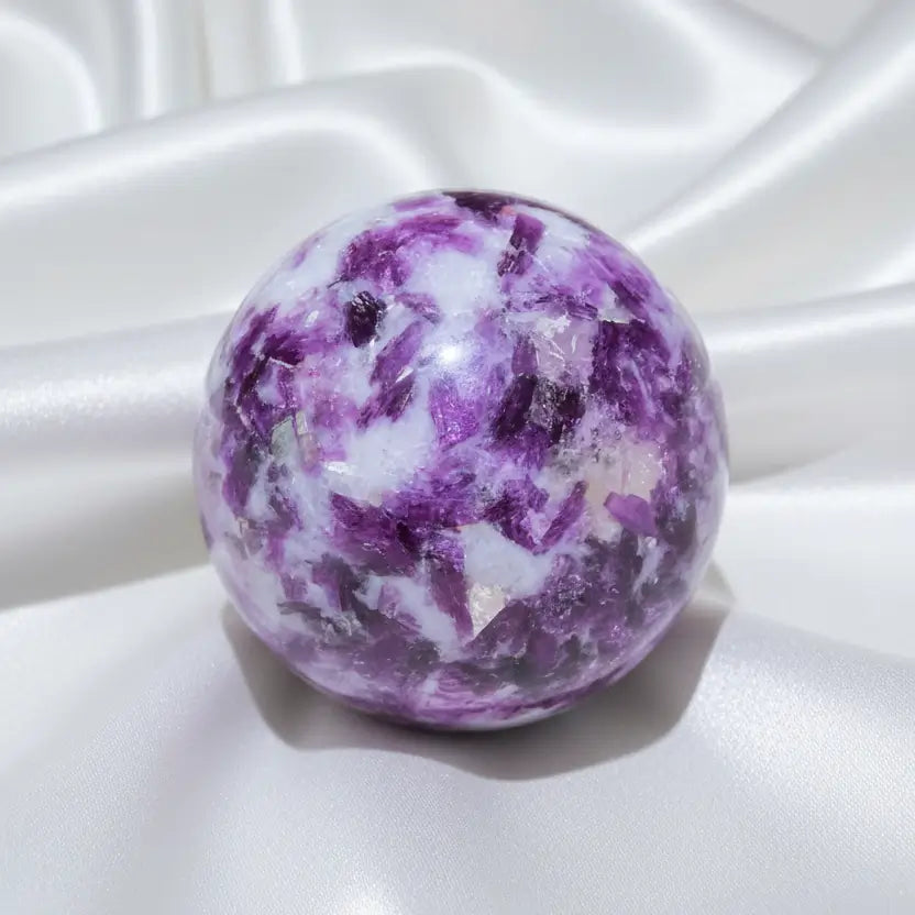 A polished lepidolite crystal sphere with a marbled pattern of purple, white, and pinkish tones