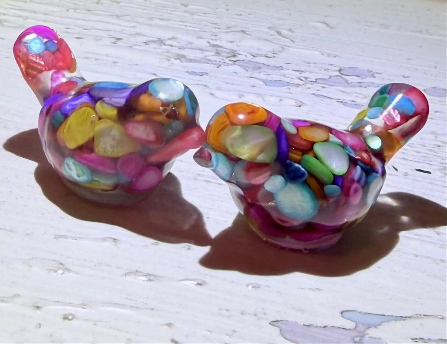 close-up set of two organite like birds, resin filled with dyed agate gravel and gold tone metal shavings on a table