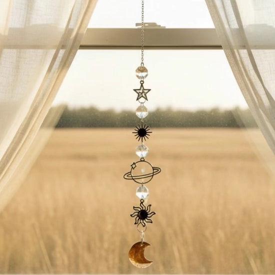 Suncatcher in a window open curtains with a hay field behind breeze blowing the suncatcher