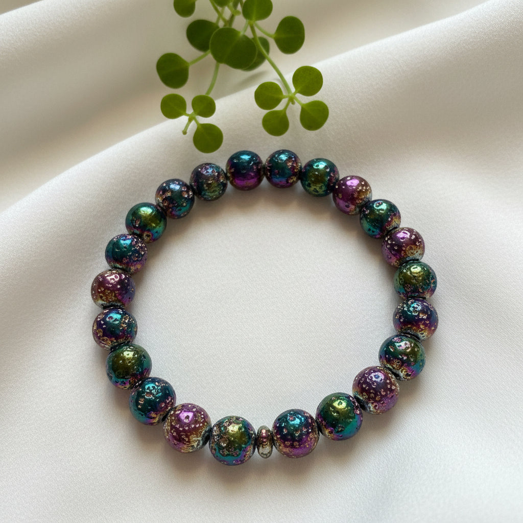 photo of a rainbow aura 9mm bead bracelet on a soft pale fabric with a small green branch behind amazing vibrant rainbow colors 