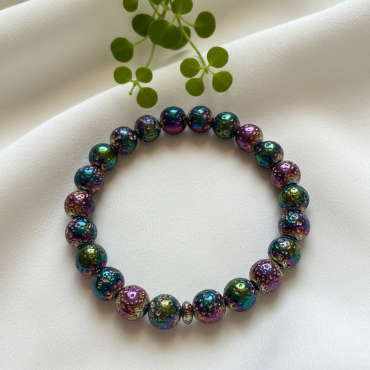 photo of a rainbow aura 9mm bead bracelet on a soft pale fabric with a small green branch behind amazing vibrant rainbow colors 