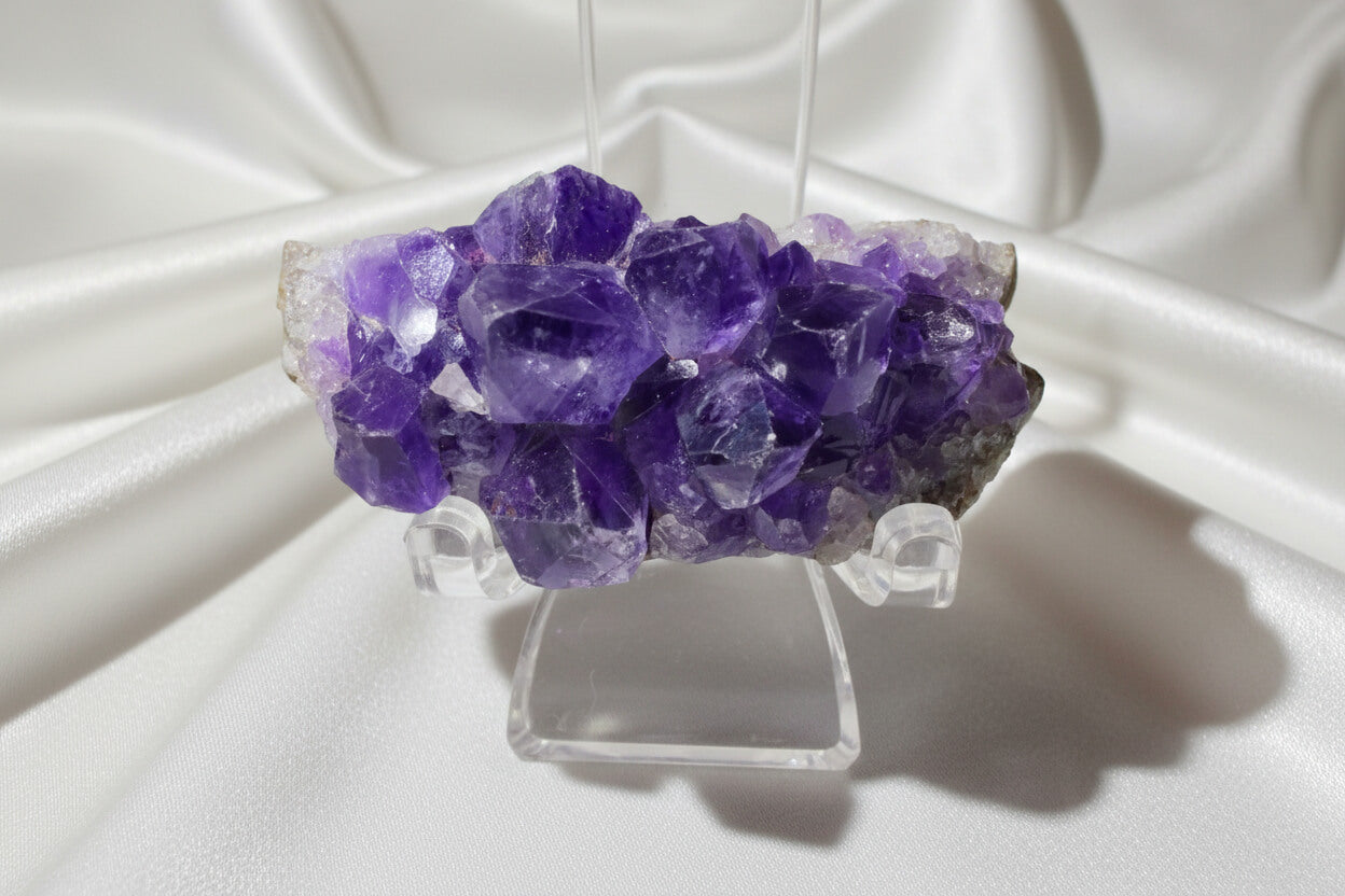 A purple amethyst crystal cluster mounted on a clear acrylic display stand, photographed against a plain light background.