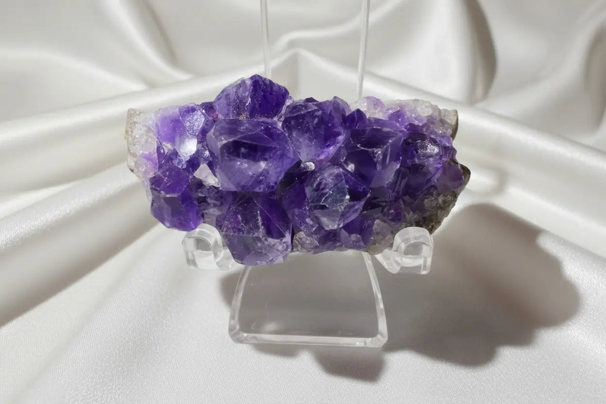A purple amethyst crystal cluster mounted on a clear acrylic display stand, photographed against a plain light background.