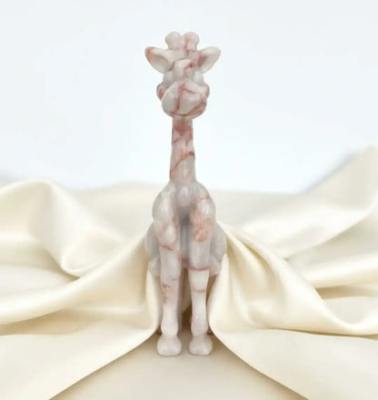 A small sculpted giraffe figurine in pale pink and white marbled stone, standing upright on a cream satin fabric backdrop against a light gray background.