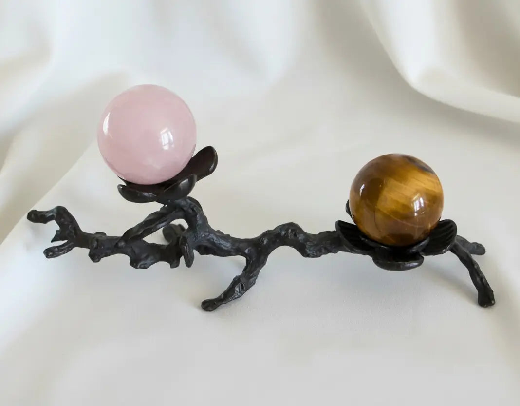 close up of two spheres on a black iron stand. rose quartz pink and tiger’s brown with stripes 