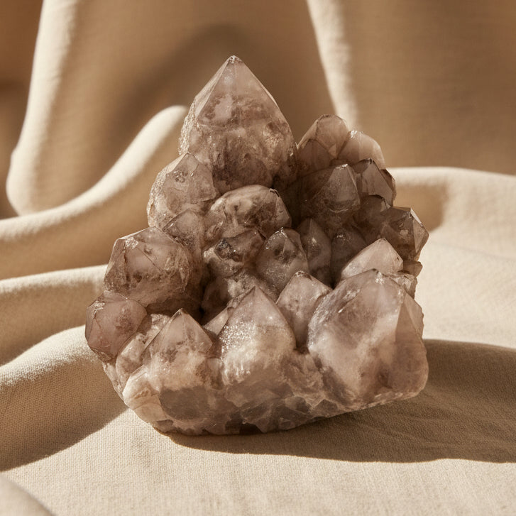 A natural smoky quartz crystal cluster with multiple pointed and jagged facets, resting on a white surface 