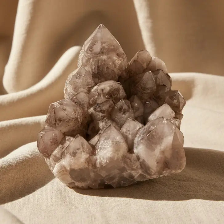 A natural smoky quartz crystal cluster with multiple pointed and jagged facets, resting on a white surface 