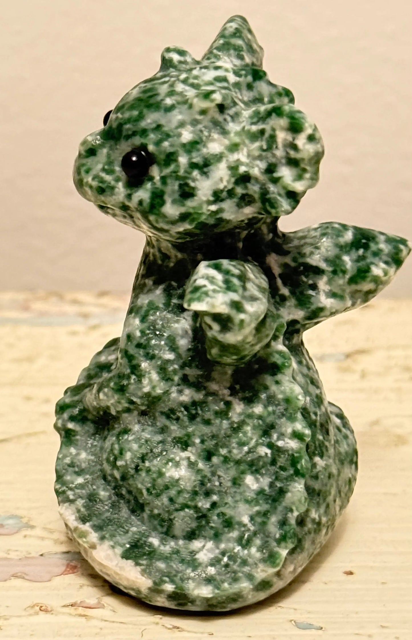 side view tree agate baby dragon carving. dark greens and off white on a table with a light background