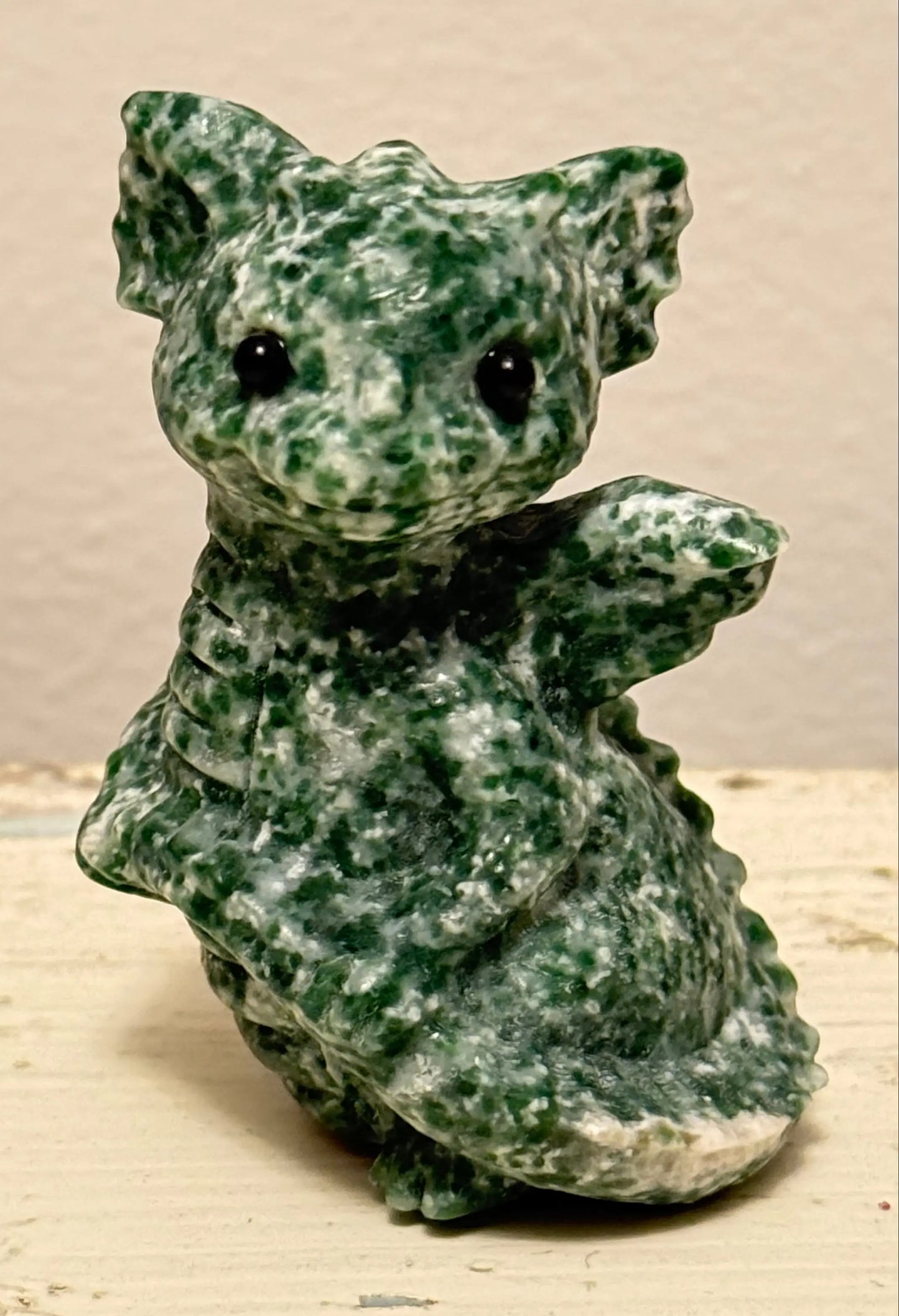 close up deep green and off white colors.  tree agate carved baby dragon on a table with a light background 