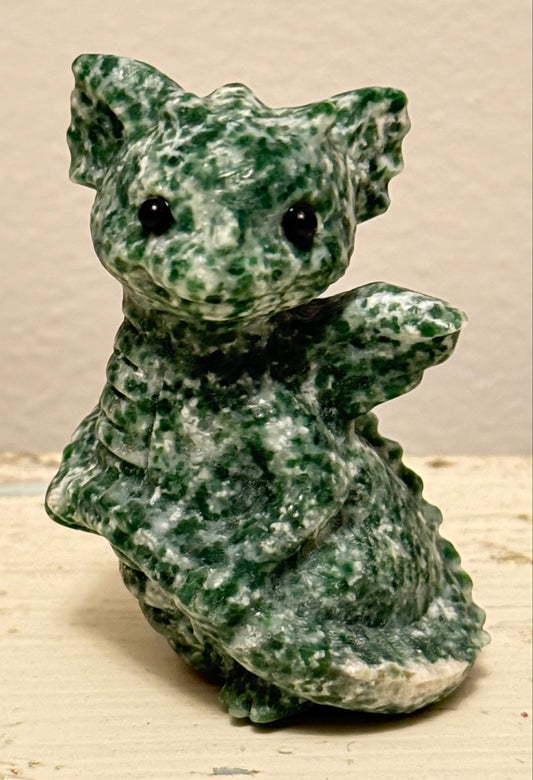 close up deep green and off white colors.  tree agate carved baby dragon on a table with a light background 