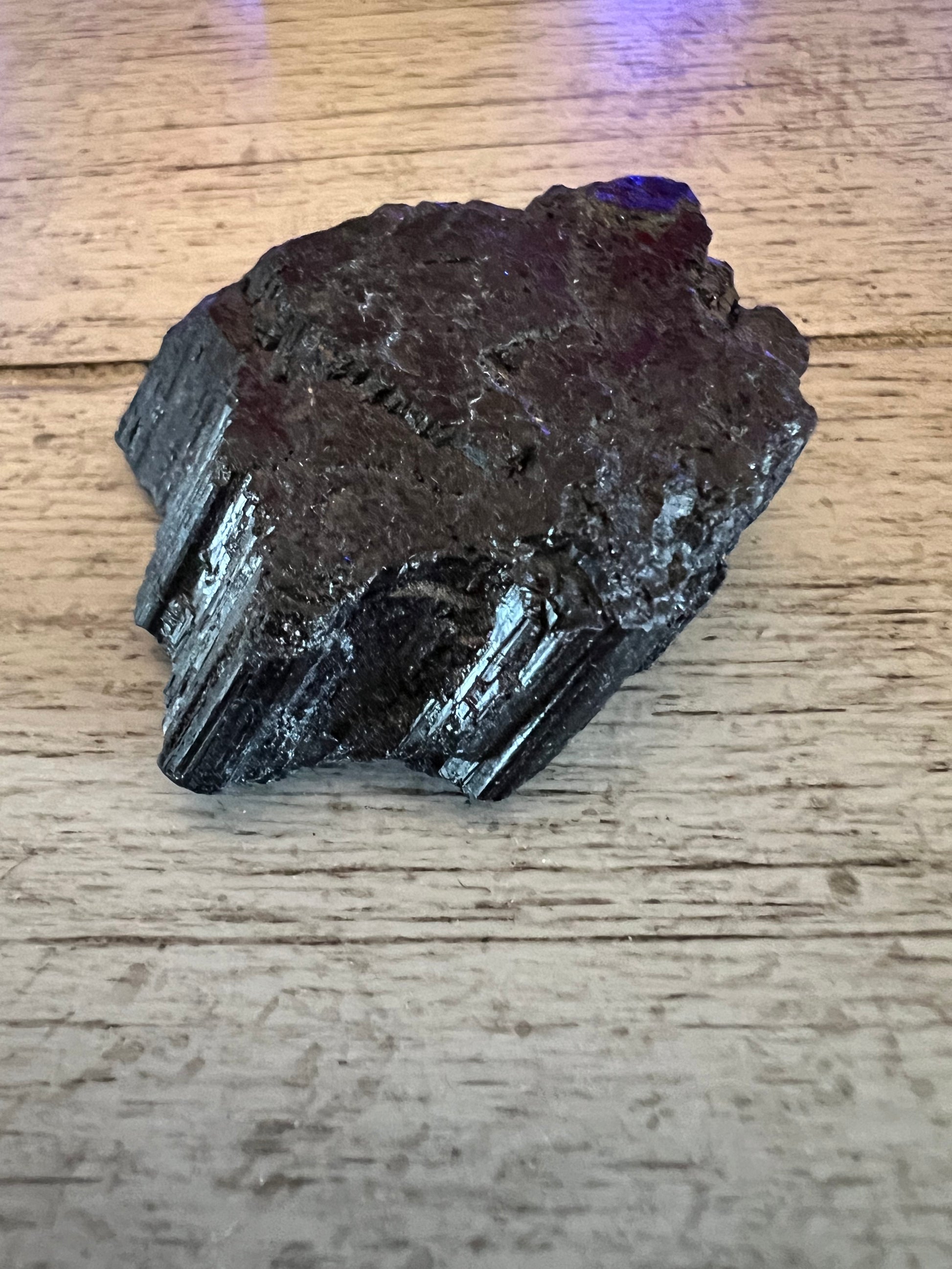 Black tourmaline stone on a wood surface.
