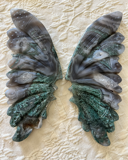 Two carved agate butterfly wings on a textured white surface.