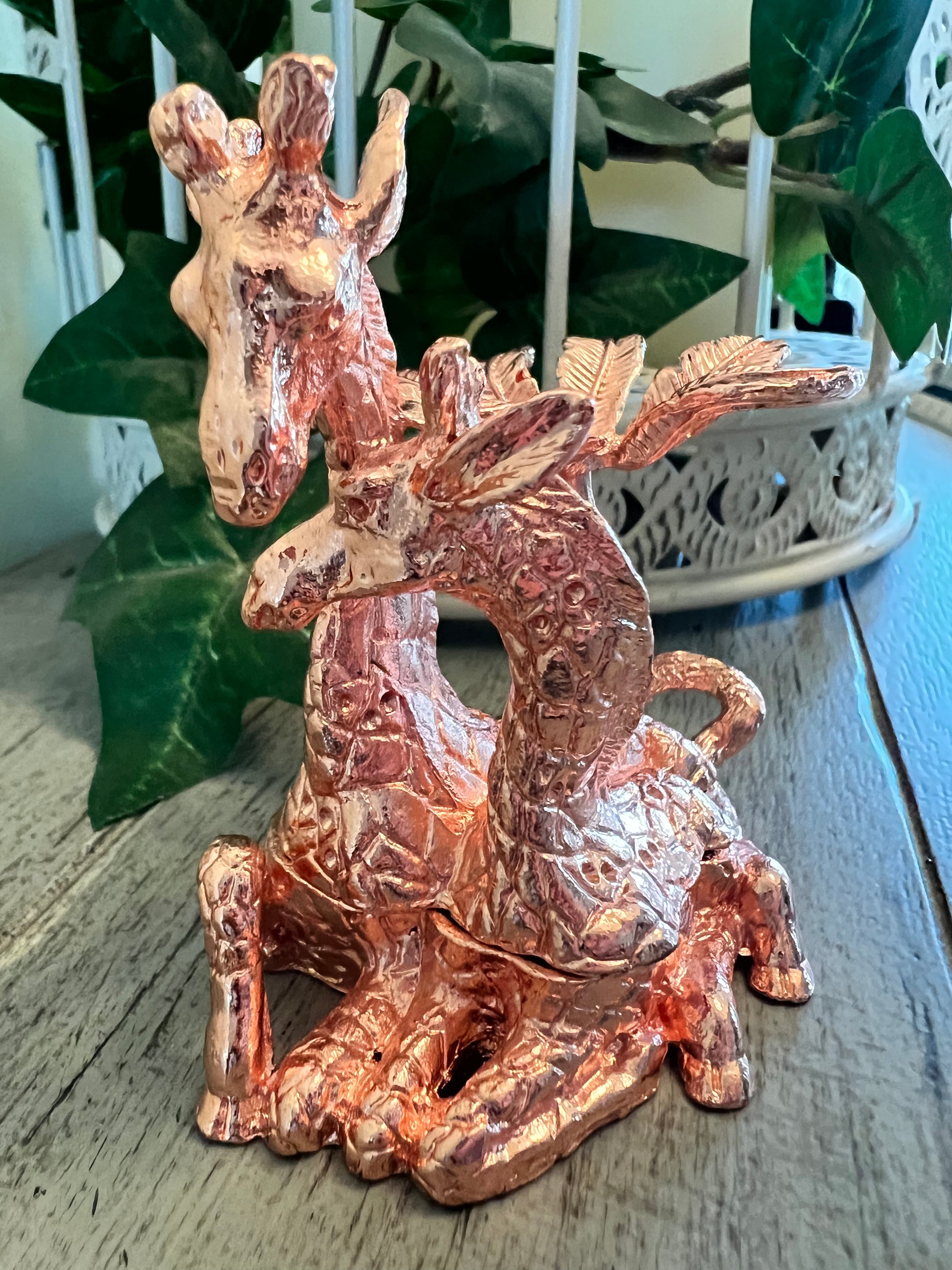 Close-up of a copper-colored giraffe sculpture on a wooden surface.