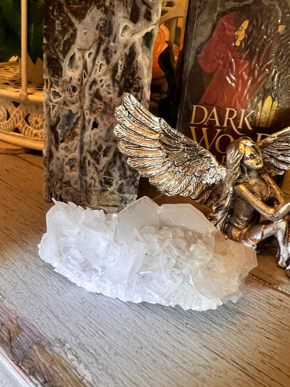 Close-up of a white quartz crystal cluster beside a silver angel figurine and a book titled "Dark Wood."