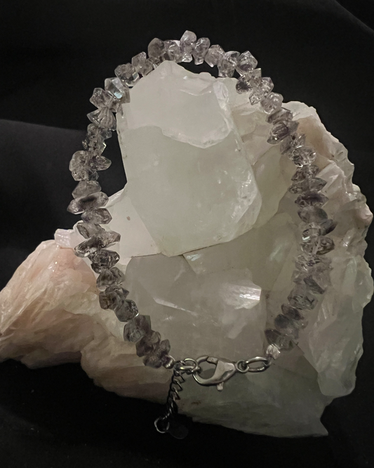 A bracelet made of raw diamonds draped over a cluster of quartz.
