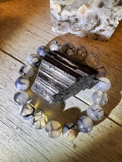 A tourmaline crystal surrounded by gray and white crackle agate beads on a wood surface with a white stone in the background.