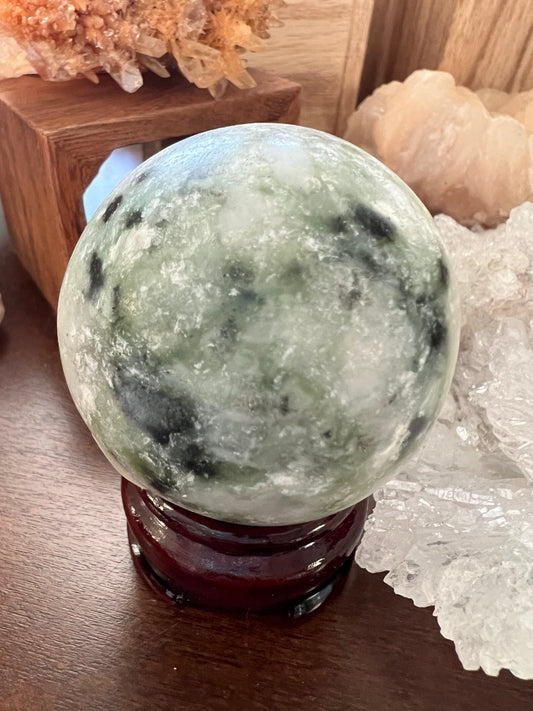 Jade orb on a dark red wooden stand, next to crystals.

