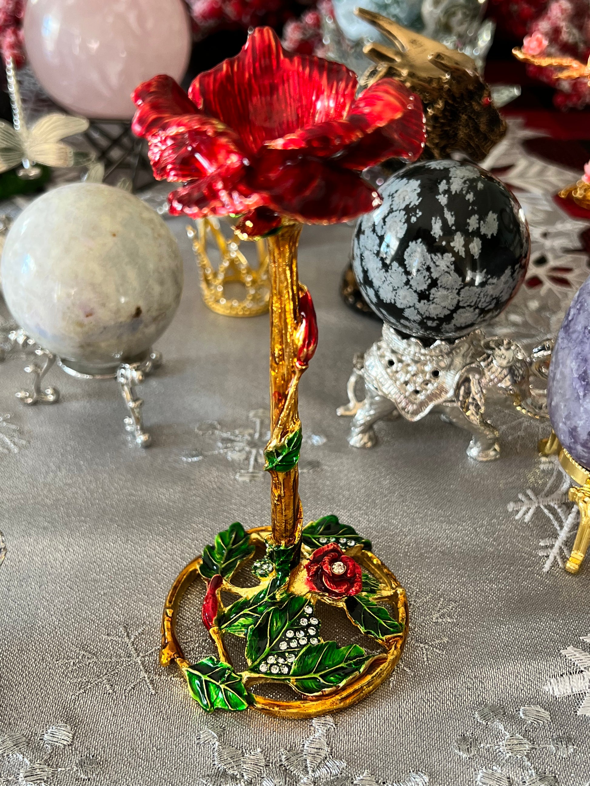 Close-up of a decorative red rose jewelry box with gold and green accents, surrounded by crystal spheres on embellished stands.
